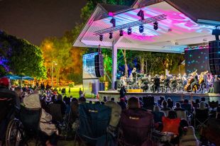 Audiences members watch on as the Queensland Symphony Orchestra perform in a park in Gladstone, Queensland, on a brightly-lit outdoor stage.