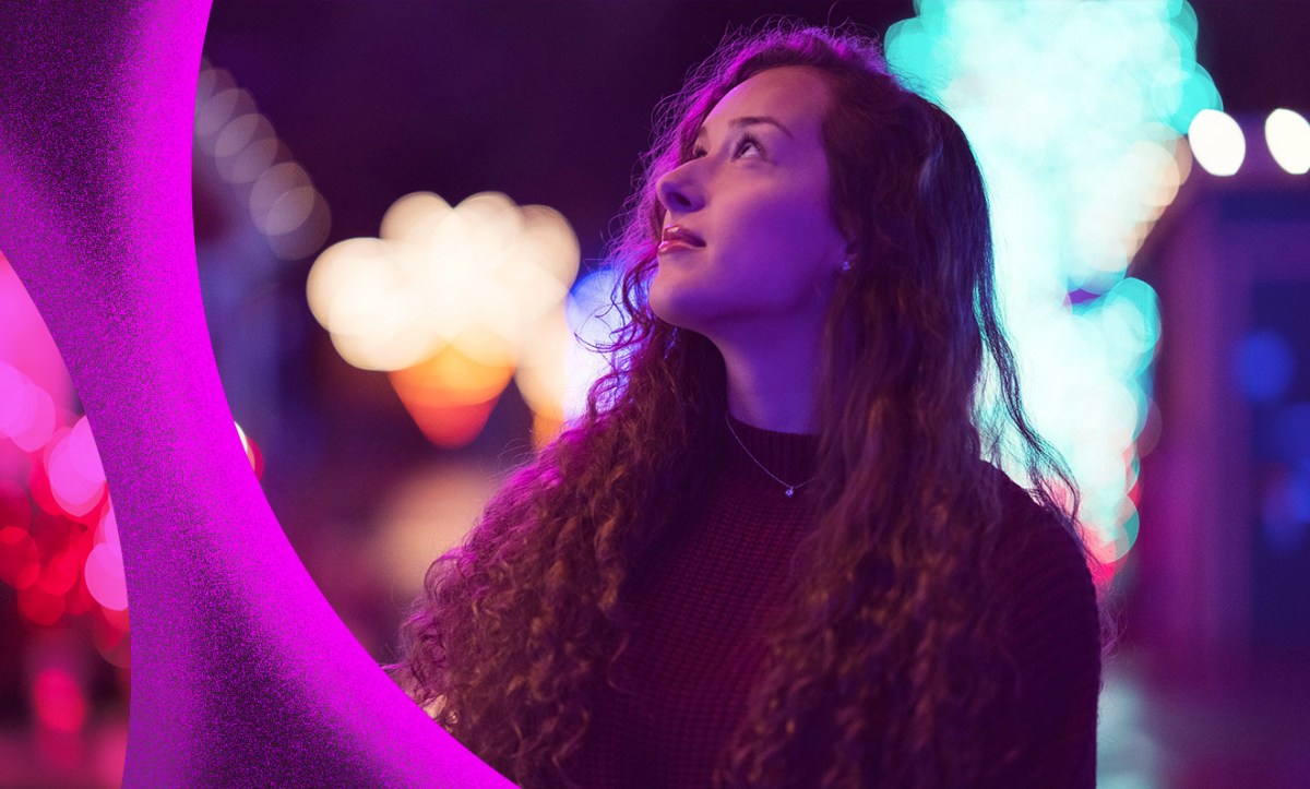 Young woman looking up with a sense of possibility, backlit by evening lights.