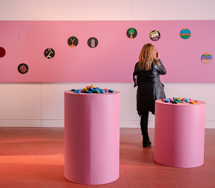 Woman looking at art in gallery with pink wall and pedestals.