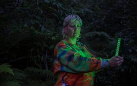 Bundanon Artist in Residence program open for applications. Image: 2023 Bundanon resident, Yandell Walton, 'Portrait Bundanon', 2023. Photo: Jodie Whalen. A woman with blond hair in a dark and slightly creepy outdoor landscape, holding a green light to her face.