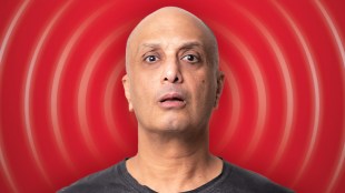 A headshot of a bald headed man of Egyptian heritage, wearing a black T shirt, against a red backdrop with curved lines emanating from his head to look as if he is broadcasting/radiating.