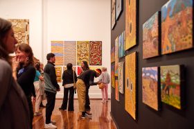 Revealed. Image is of people in a gallery looking at Aboriginal paintings on the walls.