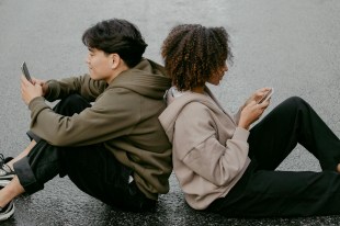 man and woman sitting back to back looking at their phones. News.