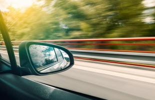 A blurred road and landscape seen from the window of a fast moving car.