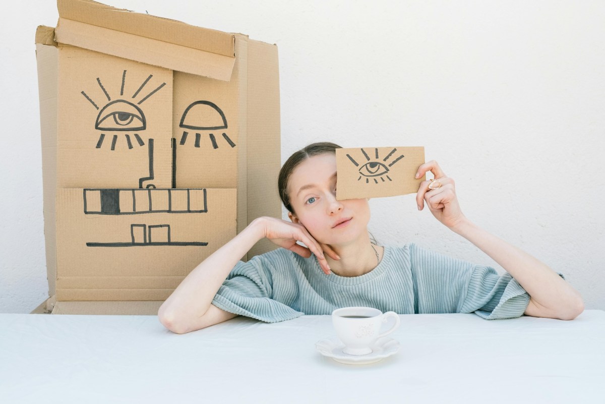 Girl holding up drawing of face on cardboard, white background. Mental Health. Art therapy.