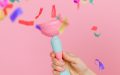 Photo: Anna Shvets, Pexels. A hand reaching out from the right hand corner of the image holding a trophy in baby pink and blue. There is confetti in the air and the background is also pink.