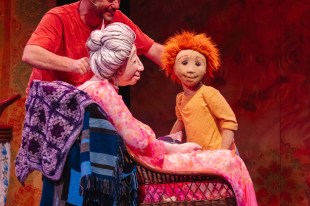 A person in an orange top manipulates two puppets - an old woman in a wicker chair and a young boy with a yellow jumper and orange hair. Wilfrid Gordon McDonald Partridge