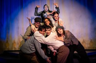 The Grinning Man. A huddle of seven young actors in vaguely Victorian/Edwardian clothing grasp and peer over each other with manically grinning faces.