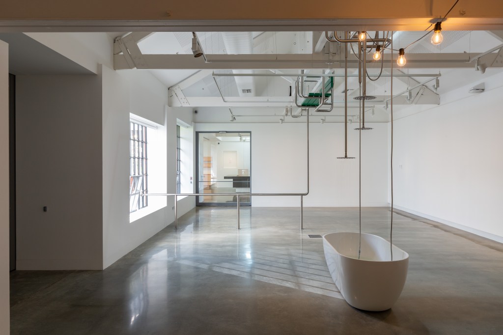A gallery with a bathtub under various pipes and shower heads.
