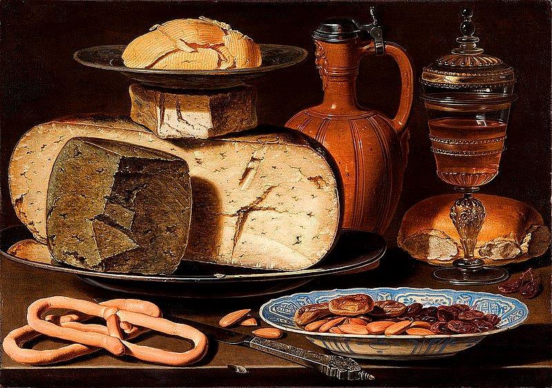 A still life painting of food, including large cheeses, a flagon, almonds, pretzels and an ornate glass vessel. The art of the table.
