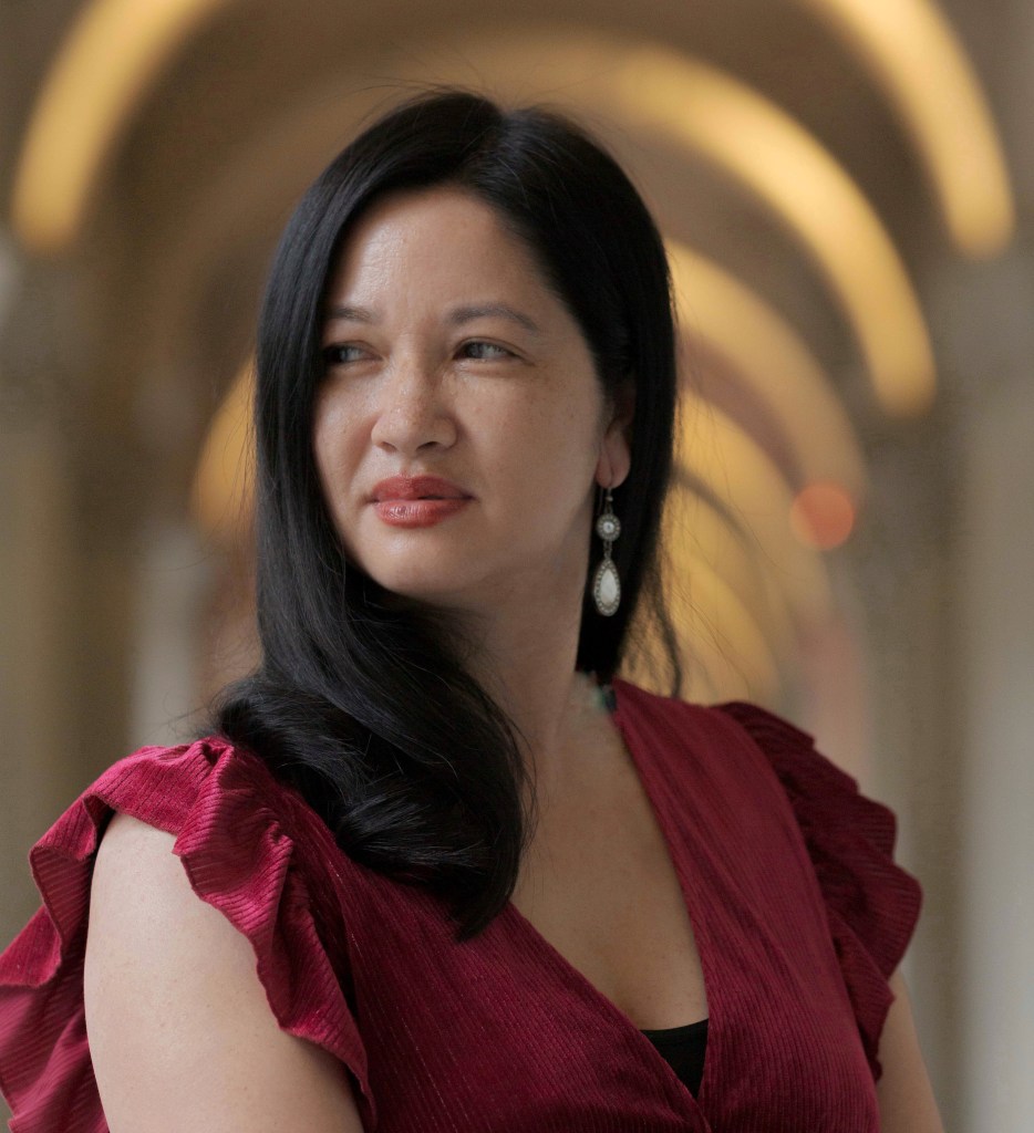 Poetry. A glamorous woman of Vietnamese appearance wears a sleeveless red dress and has her long black hair elegantly styled. One drop earring is uncovered and she is looking off to the left with a slight smile.