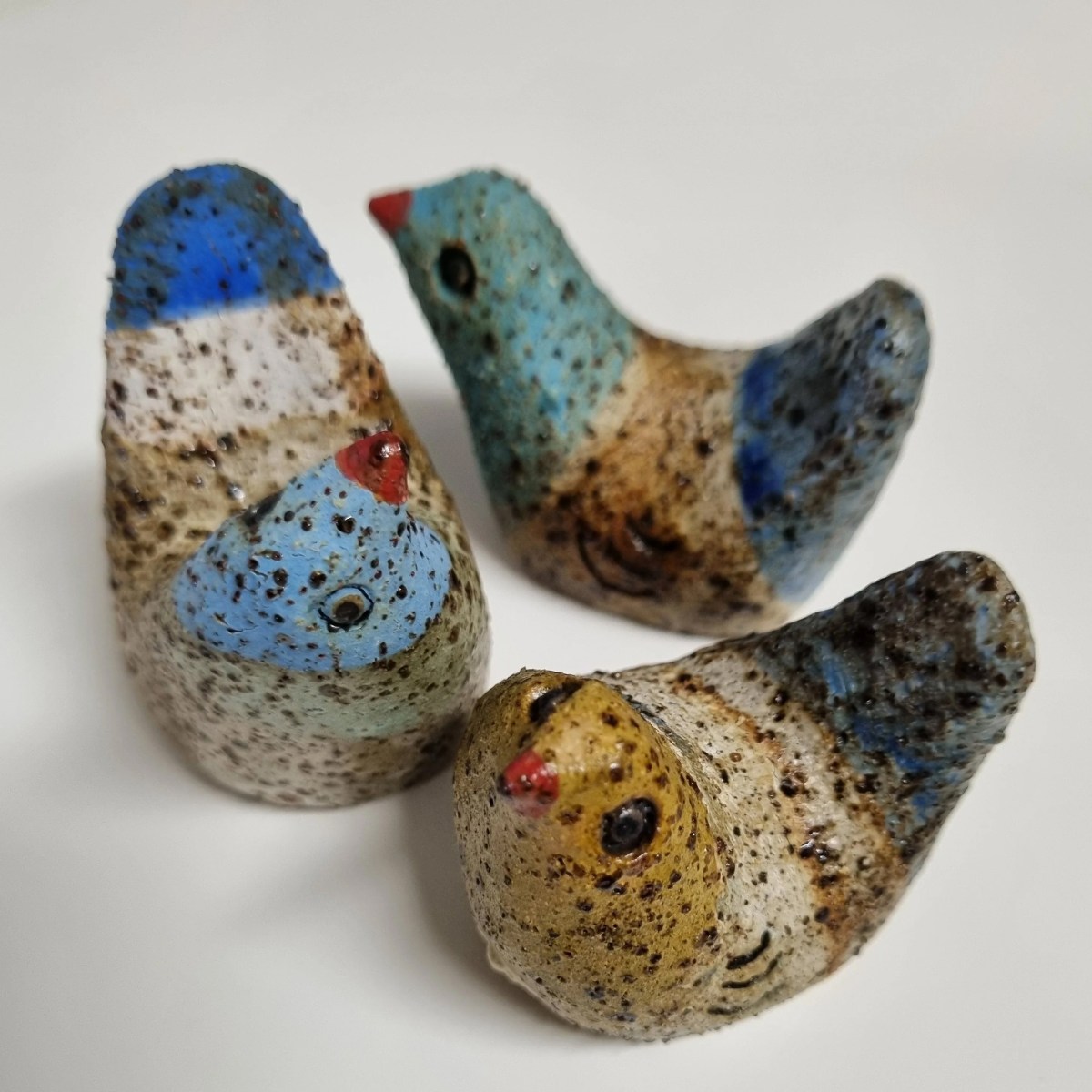 gallery gift shop. Three little ceramic birds with no wings, looking upwards and painted in stripes of blue, white, turquoise and yellow, and dotted with brown speckles.