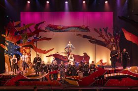 A stage filled with performers dressed as animals and birds with a backdrop and set covered in Aboriginal designs.