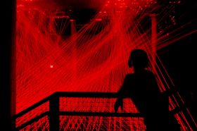 Illuminate Adelaide. A silhouetted figure gazes at an art installation comprising red threads of light in a large dark space.
