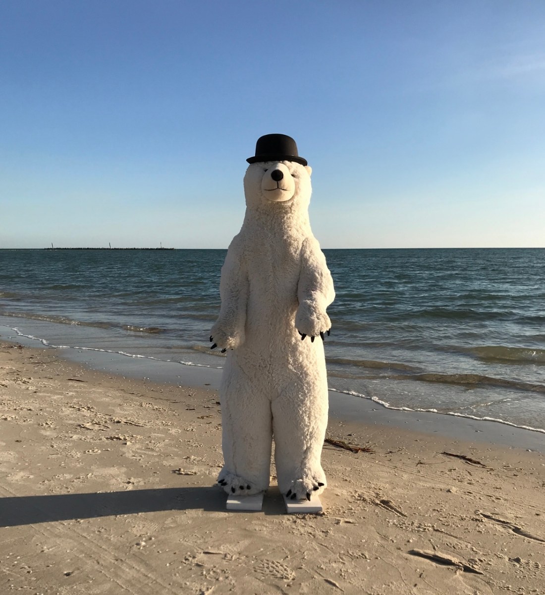 gallery gift shop. Tall stuffed polar bear toy standing on a beach wearing a bowler hat.