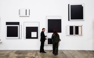 Sydney Contemporary 2024 to return to Carriageworks 5-8 September. Photo: Supplied. Two figures wearing black in conversation, standing in front of a wall of black and white paintings.