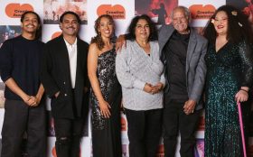 2024 First Nations Arts and Culture Awards recipients (l to r) Dean Brady, Tibian Wyles, Sara Prestwidge, Brenda Gifford, Uncle Badger Bates, Meleika Gresa. Photo: Supplied. A group of First Nations artists in front of a photo board with the Creative Australia logo and photos of First Nations performances.