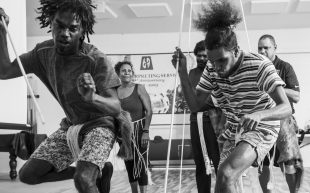 Deaf Indigenous Dance Group dancers Leslie Footscray, Nathaniel Murray and others rehearsing in Cairns, 2021. Photo: Sean Davey. A black and white photo of First People dancers rehearsing in a room.