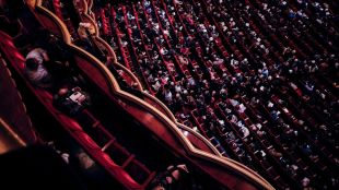 Theatre access: A bird's eye view on the interior of a lavish theatre space showing audience members finding their seats before curtain up.