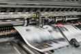 A newspaper is printed on an industrial printing press.