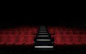 Photo: Felix Mooneeram, Unsplash. An empty theatre with red chairs.