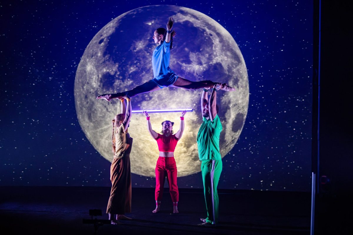 I Wish... In front of a backdrop of a huge moon in the night sky, four circus performers dressed in yellow, blue, red and green perform, with two performers holding aloft a third who is doing the splits, while the fourth performer stands at the back holding up an Astera light tube.