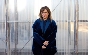 25th Biennale of Sydney Artistic Director, Hoor Al Qasimi. Photo: Dan Boud. A woman with light brown skin, gradient brown hair, wearing lipstick, a blue velvet blazer and smiling at the camera.