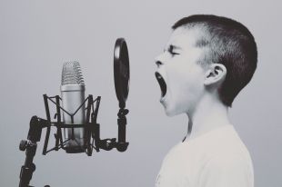 A black and white photograph pf a young boy singing into a microphone in a recording studio.