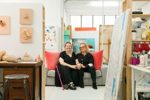 Founders of Here Space, Michelle Vine and Perrin Ellis. Photo: Claudia Baxter. Two people sitting on a sofa in the middle of a brightly lit studio space.