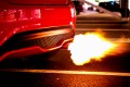 A car backfiring on the road at night, a flash of flame emerging from its exhaust.