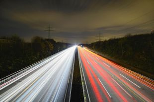 A highway at night. On the left hand side, the blurred and speeding white-coloured headlights of cars race toward the camera. On the right, red taillight trails recede into the distance.