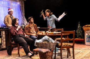 Never Closer. Four student looking types lounge around a shared house set at Christmas time. One woman brandishes a bottle towards a man and a woman sitting at a table. A fourth man leans to the side wearing a Santa hat.