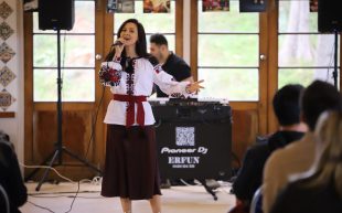 A performer at Spirit of Welcome Community Festival 2023. Photo: Damon AMB. A woman with long brown hair wearing a white top with floral embroidery singing at the front of a seated crowd.