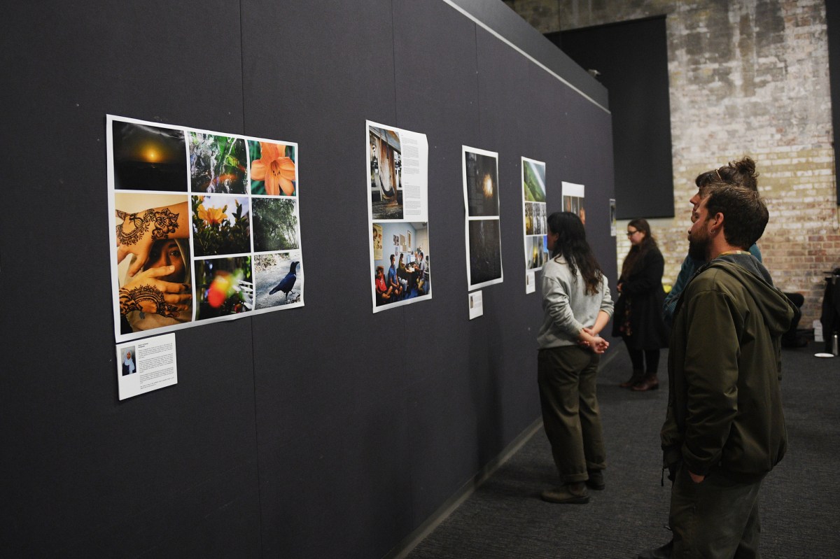 Homelands Regional Arts Tour 2023. Photo: Danish Ravi. Photographic works displayed on a black panel with people looking at the works.