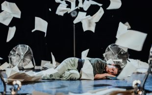 'Little Murmur' to tour in Australia. Photo: Angela Grabowska. A young woman lies on the stage with a book in her hand and pages flying in the air.