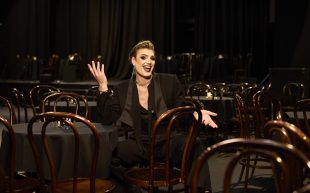 Adelaide Cabaret Festival 2024 Icon Award winner, Reuben Kaye in Space Theatre, Adelaide Festival Centre. Photo: Claudio Raschella. Kaye is in a black suit set with a low neckline, wearing heavy makeup and his hair sleeked back. He is sitting down with a big smile and gesturing with his hands.
