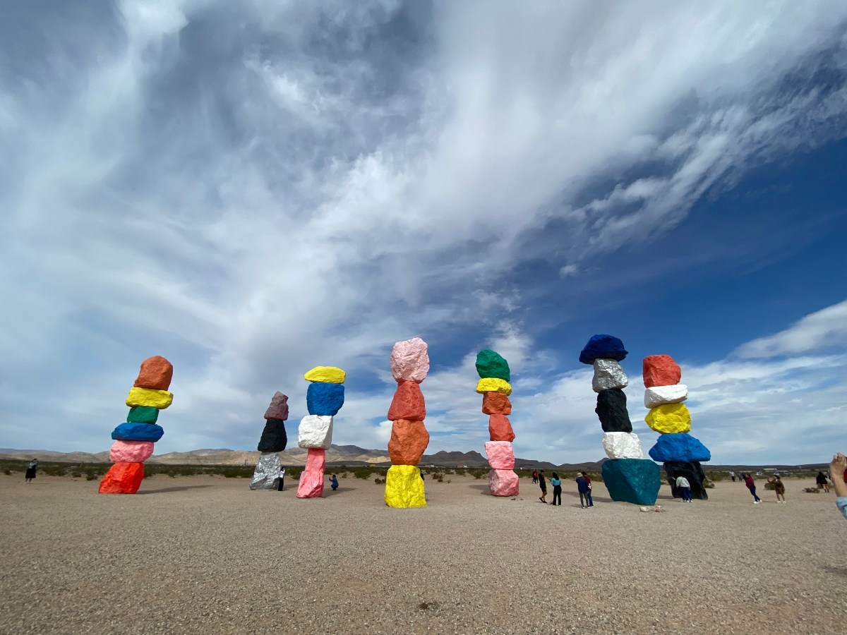 Nevada Art Trail. Seven columns of big brightly coloured rocks piled on top of each other in the desert. People are milling around the bottom to give an idea of scale.