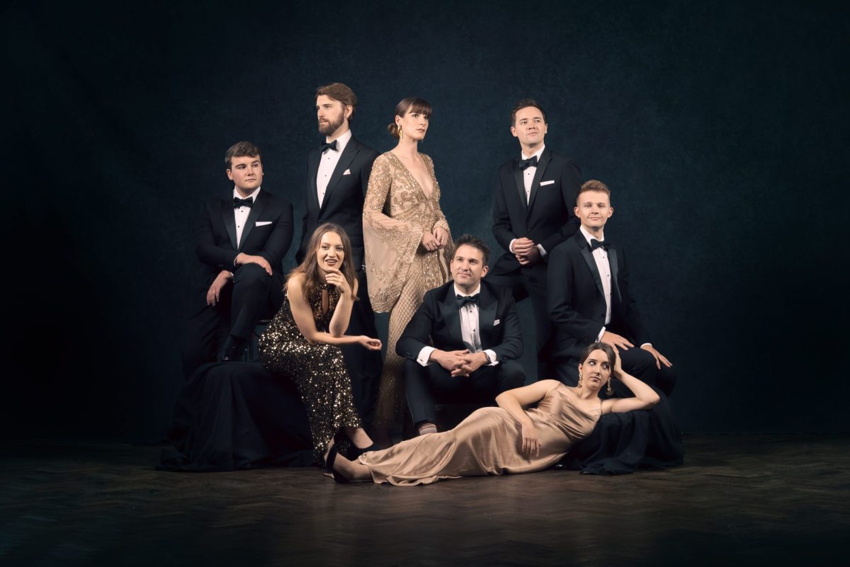 A group photo of five men in tuxedos and three women in formal tan-coloured evening wear.