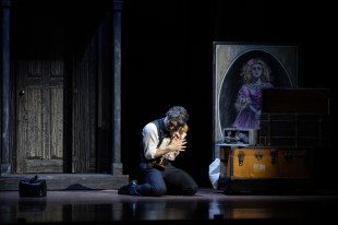 A man is kneeling in the middle of a stage, craddling a toy girl. He looks distraught.