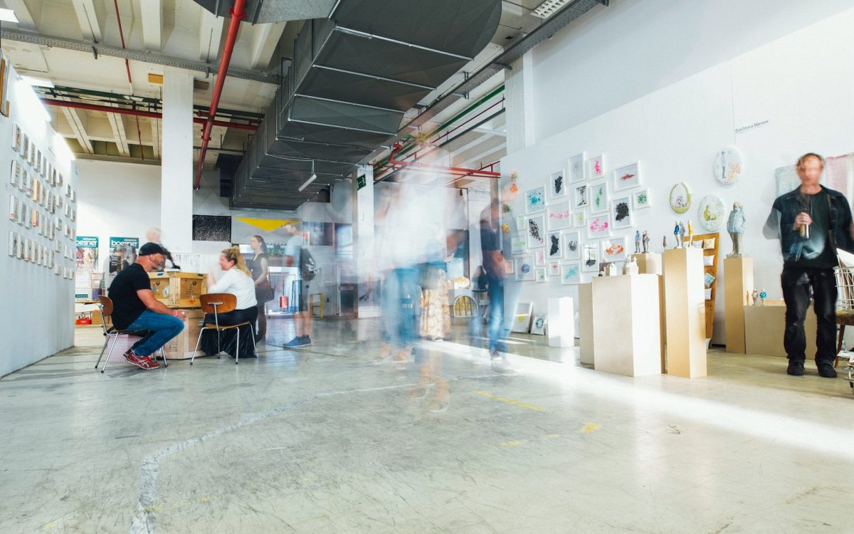 Photo: Markus Spiske, Unsplash. A brightly-lit space with artwork displays on walls and visitors walking about.