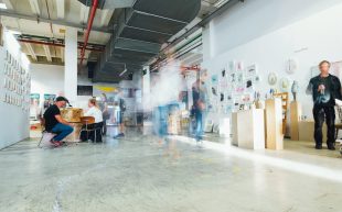 Photo: Markus Spiske, Unsplash. A brightly-lit space with artwork displays on walls and visitors walking about.