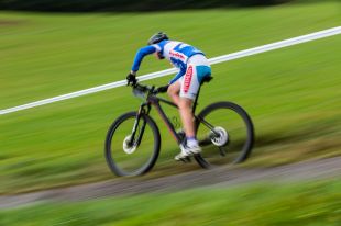Arts sector appointments. A movement-blurred image of a cyclist riding fast down a grassy hill.