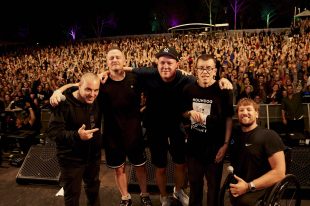 Ability Fest. Five men in black T shirts are in front of festival crowd, one on the right is in a wheelchair, smiling and holding a microphone.