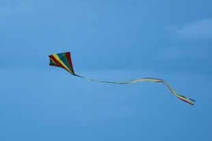 A colourfully-striped triangular kite with a long, bright tail flies against a clear blue sky.