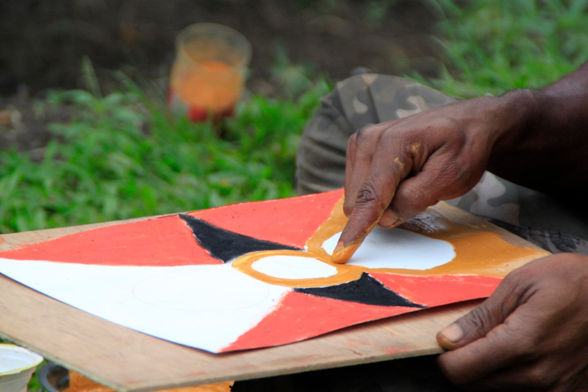 Image of hand painting a tradition shield design. APT