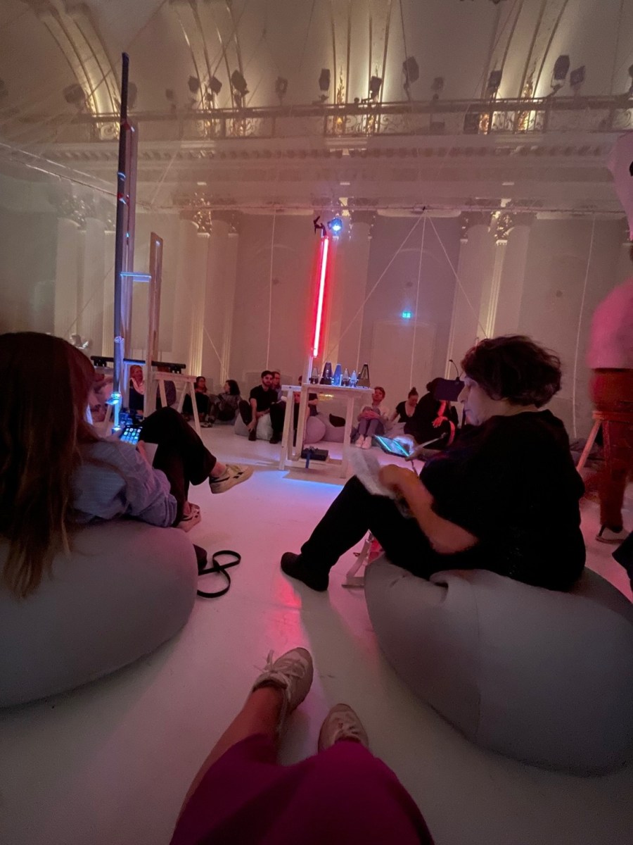 a group of people sit in a pink lit room on beanbags. culture