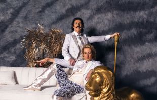 A carefully staged and rather camp photograph of two men dressed in white and lounging on a white couch. A statue of a golden lion sits beside one of the men, who are the stars of Sydney Festival's 'Siegfried & Roy: The Unauthorised Opera'.