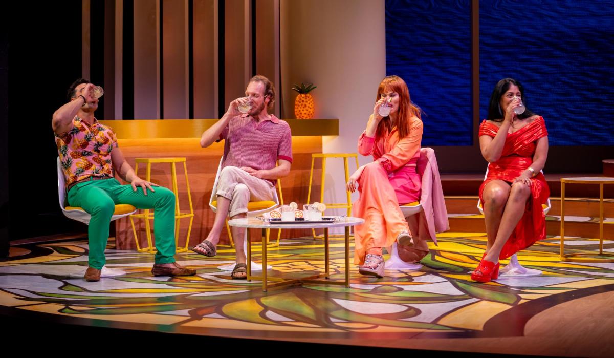 Two men and two wome are seated. All are drinking. All are wearing colourful clothes. The design colours are bright graphic prints.