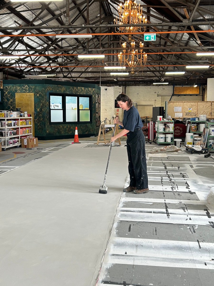 woman with paint brush on end of broom painting sets in warehouse. Opera Australia.