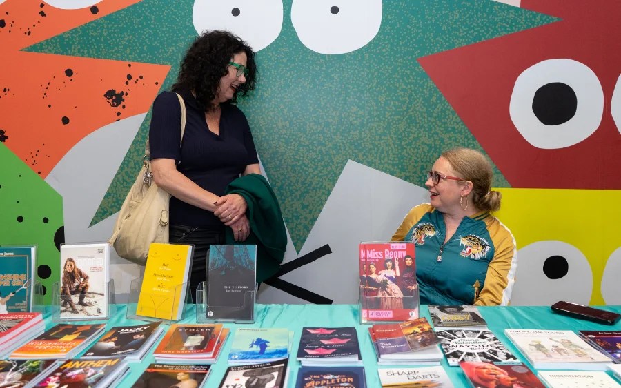 Two women at a market stall selling books. Currency Press